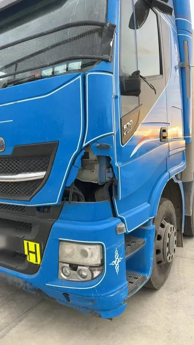 A blue Iveco X-Way truck with panel damage behind the cab door