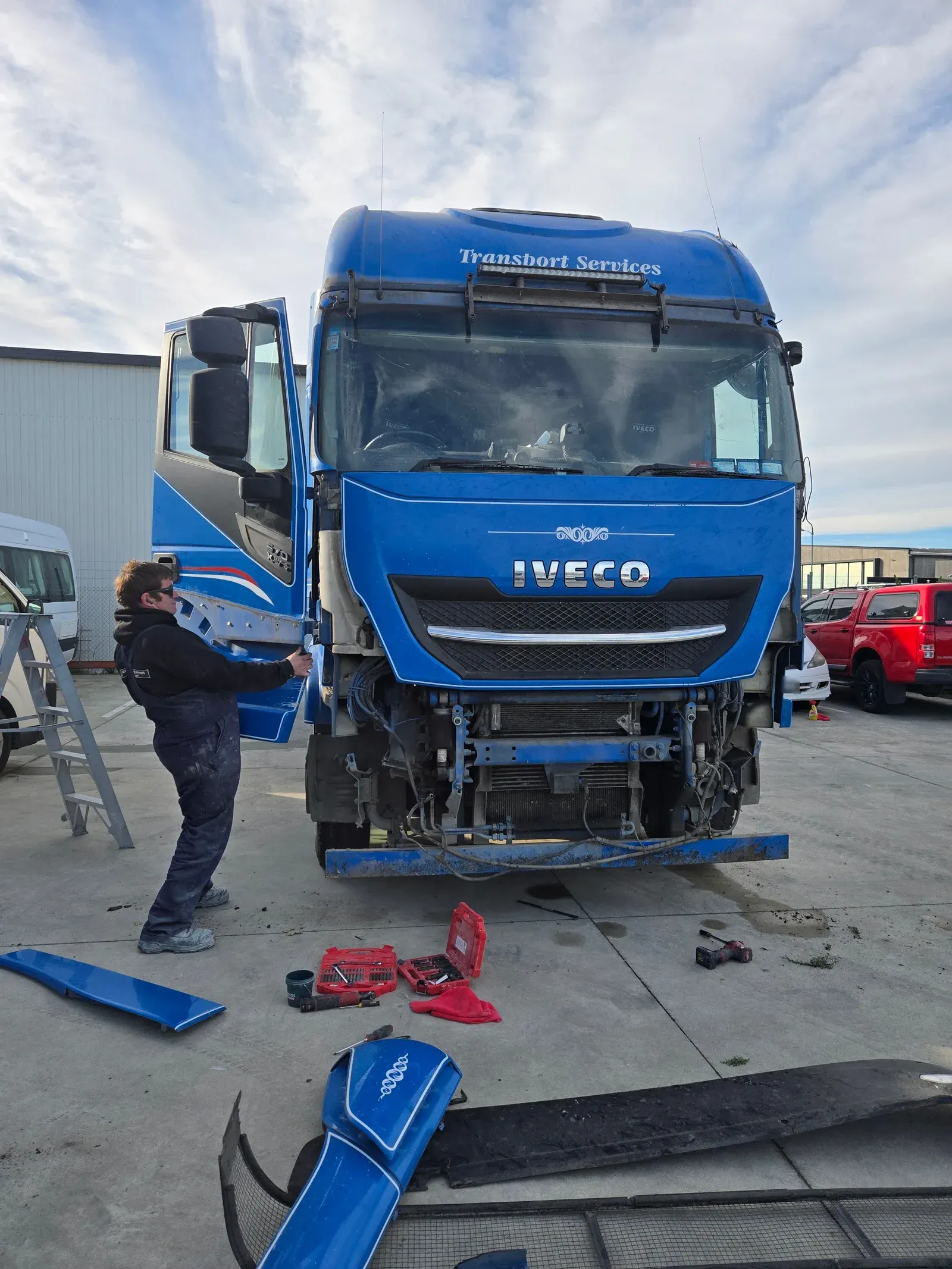 Josh stripping the front panels off a blue Iveco truck in the yard