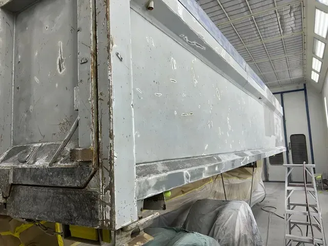 A tipper body stripped back to bare corroded steel in the spray booth